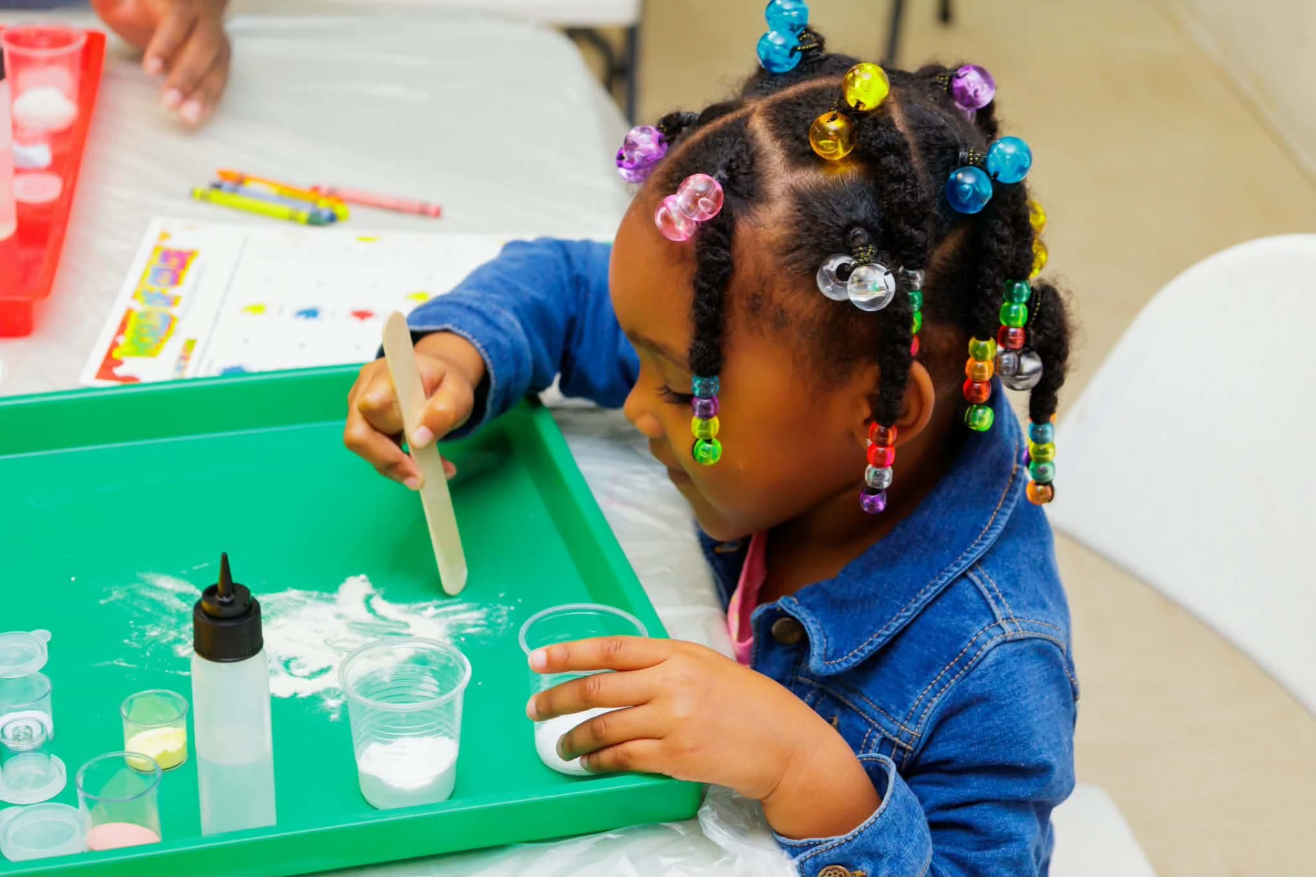 Young student stirring a science activity on a green tray during an enrichment session